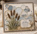 Birthday card with brown cattails, overlapping bubble circles, and lake landscape background