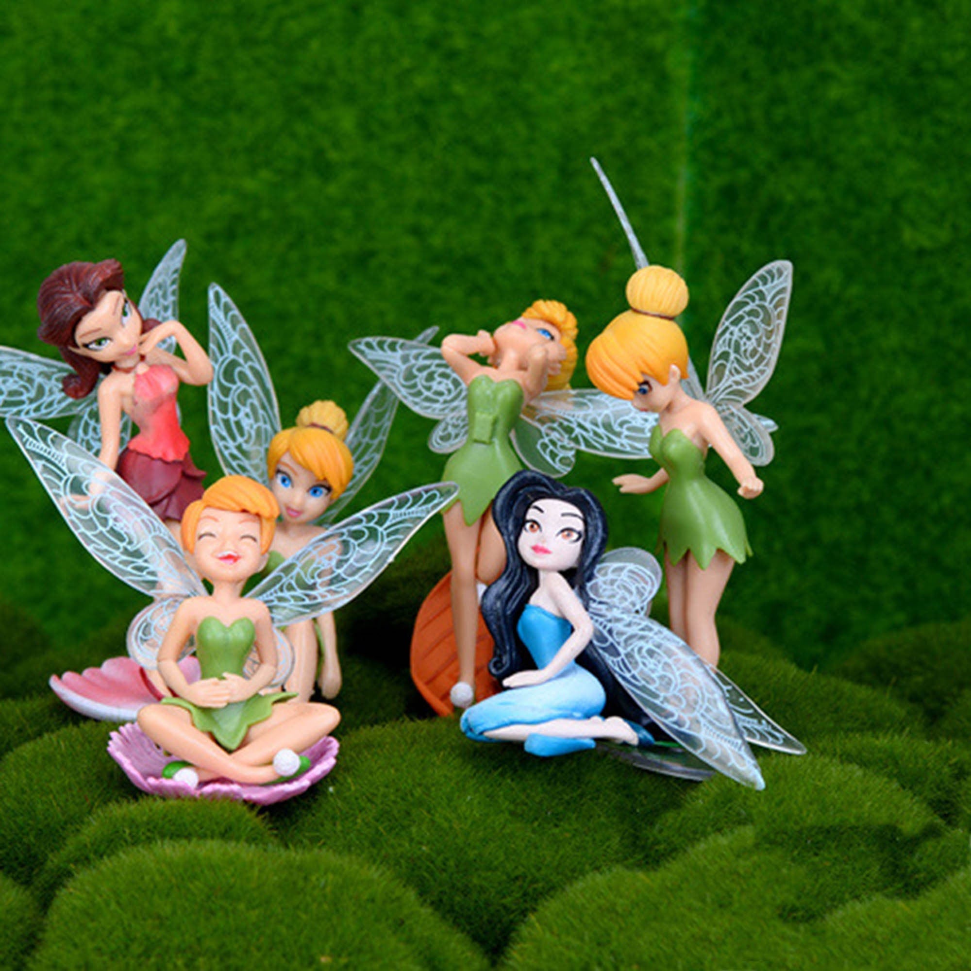 Six miniature fairy figurines with wings and colorful dresses. The fairies are posed in different positions and have different colored hair and wings. The fairies are sitting on a bed of green moss.