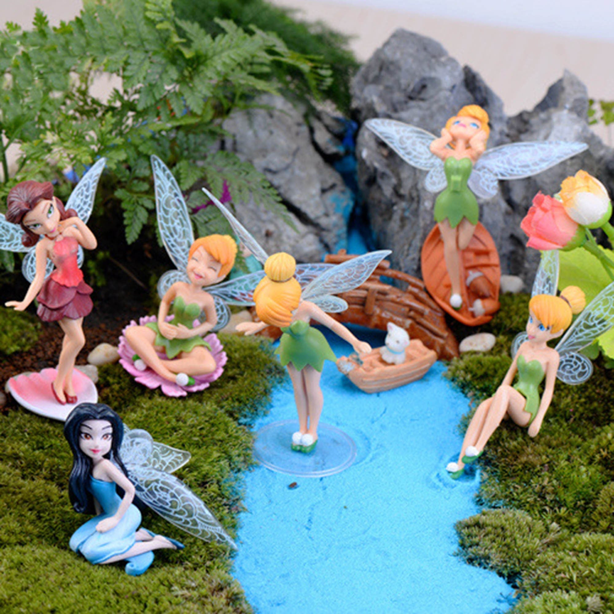 Set of six miniature fairy figurines with translucent wings. The fairies are in various poses and have different colored dresses. The fairies are sitting on a mossy surface with a small stream and a miniature bridge.