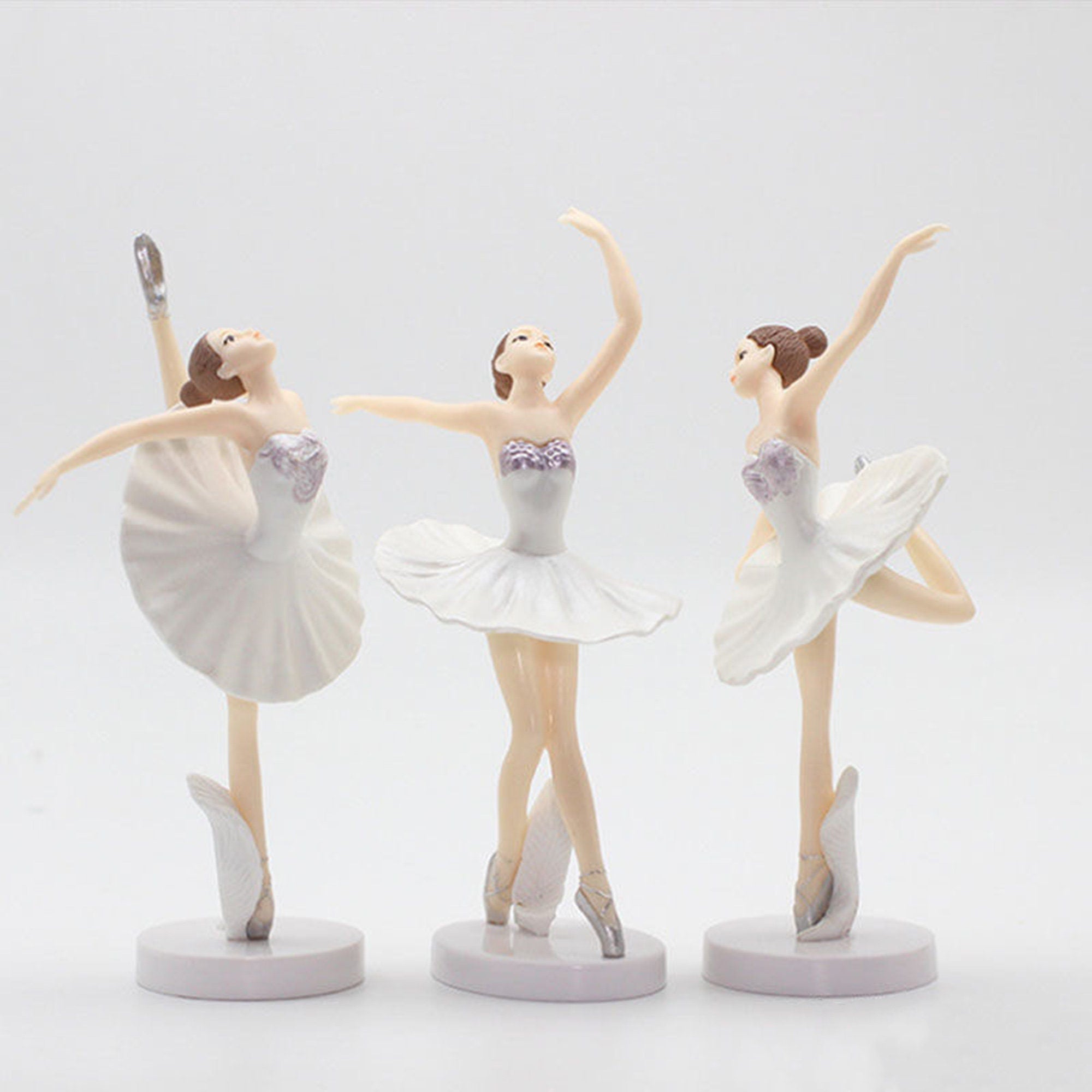 Three white ballerina figurines with purple accents on their tutus and shoes. The ballerinas are posed in different dance positions.