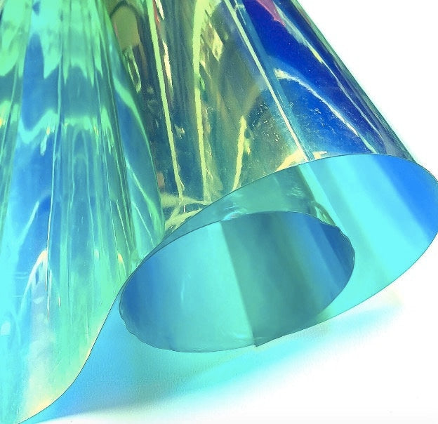 A sheet of iridescent film, displaying a spectrum of colors including blue, green, and yellow. The material is folded, creating a layered effect with varying shades and highlights. The overall appearance is smooth and reflective.